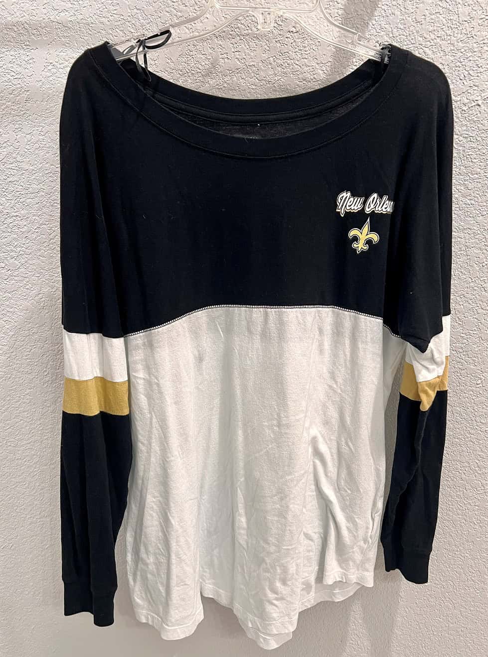 Front view of a New Orleans Saints long sleeve tee, showcasing bold ‘SAINTS’ lettering in white with gold trim on a black background.