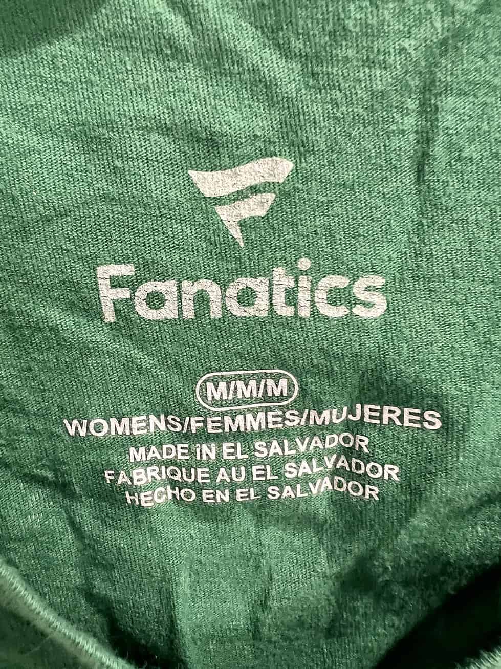 Close-up of the Fanatics brand tag, indicating the shirt’s size as Women’s Medium and origin of manufacture in El Salvador.
