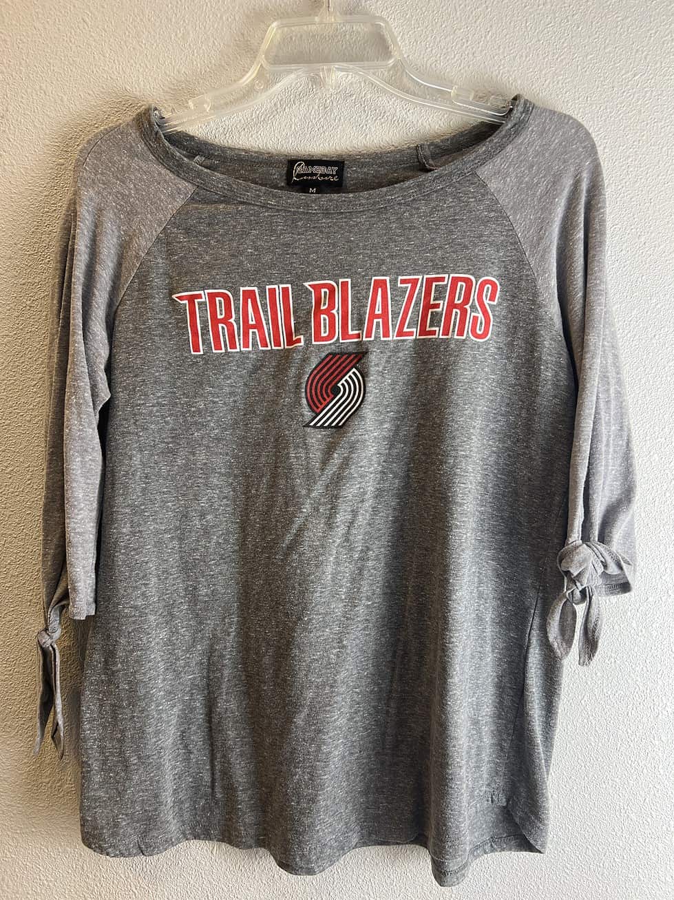 Full view of the stylish Portland Trail Blazers long-sleeve top, featuring a wide neckline, cold shoulder design with tied sleeves, and the team's iconic logo.