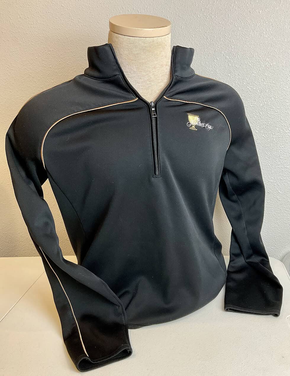 Frontal view of a black EP Pro quarter-zip sweatshirt featuring a sleek design with gold piping and an embroidered Presidents Cup logo, showcasing a sporty and professional look.