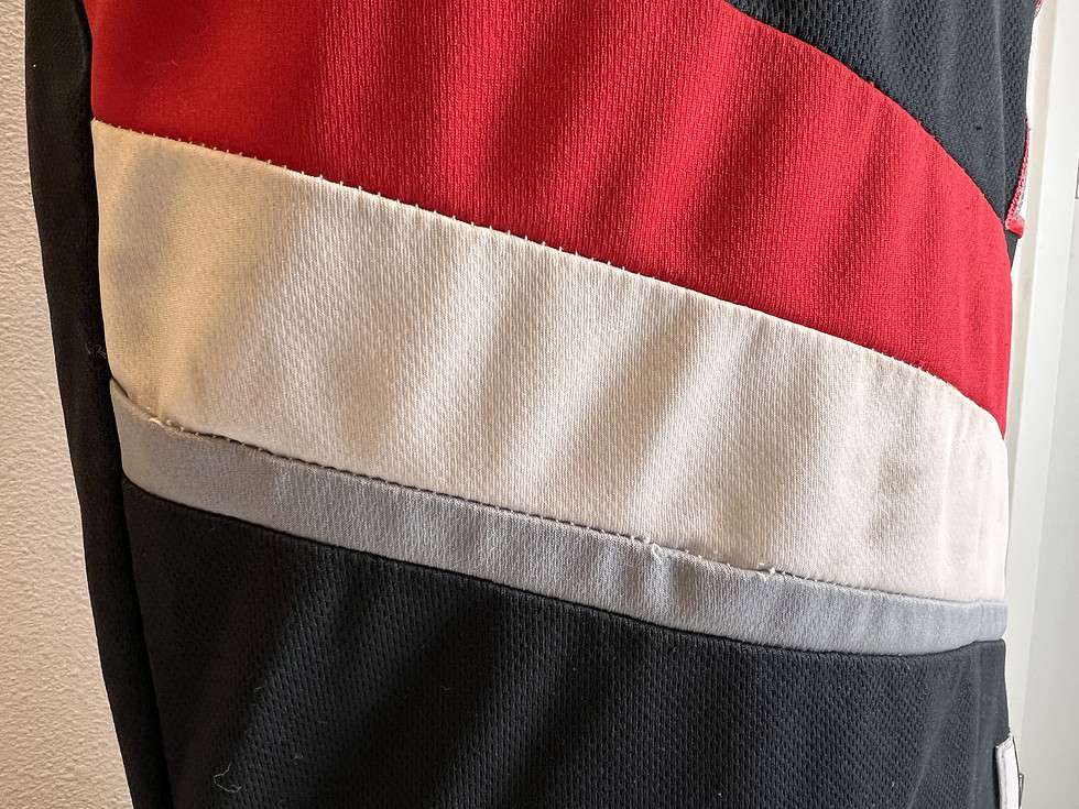 Detail of the midsection of a black Adidas Portland Trail Blazers NBA jersey, showing the red and white horizontal stripes and a small stain on the white fabric.