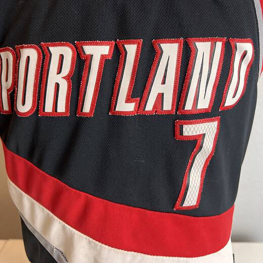 Adidas Portland Trail Blazers NBA jersey in black with red and white stripes, featuring 'PORTLAND' and the number '7' on the front, and 'ROY 7' on the back. Size tag shows 'S, Length +2'. Visible wear and staining present.