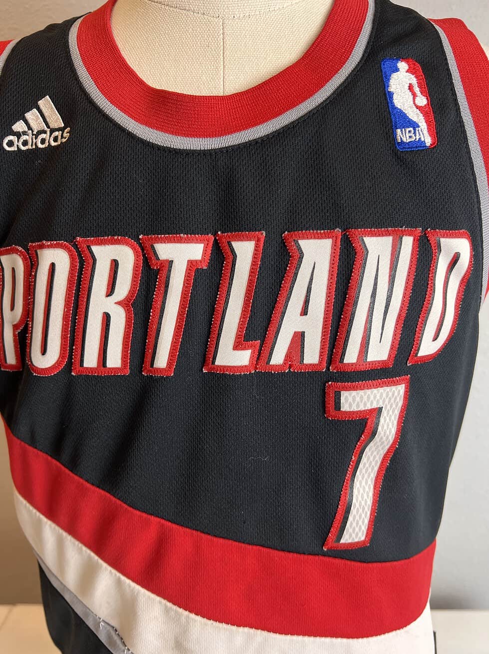 Adidas Portland Trail Blazers NBA jersey in black with red and white stripes, featuring 'PORTLAND' and the number '7' on the front, and 'ROY 7' on the back. Size tag shows 'S, Length +2'. Visible wear and staining present.