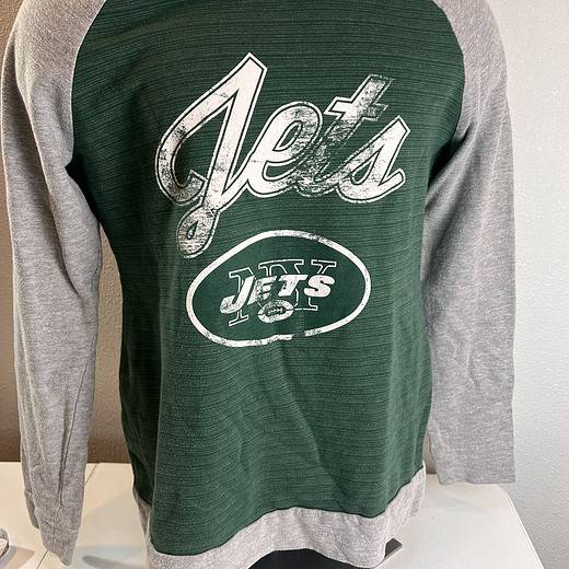 A two-toned long-sleeve sweatshirt with heather grey sleeves and a dark green torso, featuring a distressed white 'Jets' script and logo on the front.
