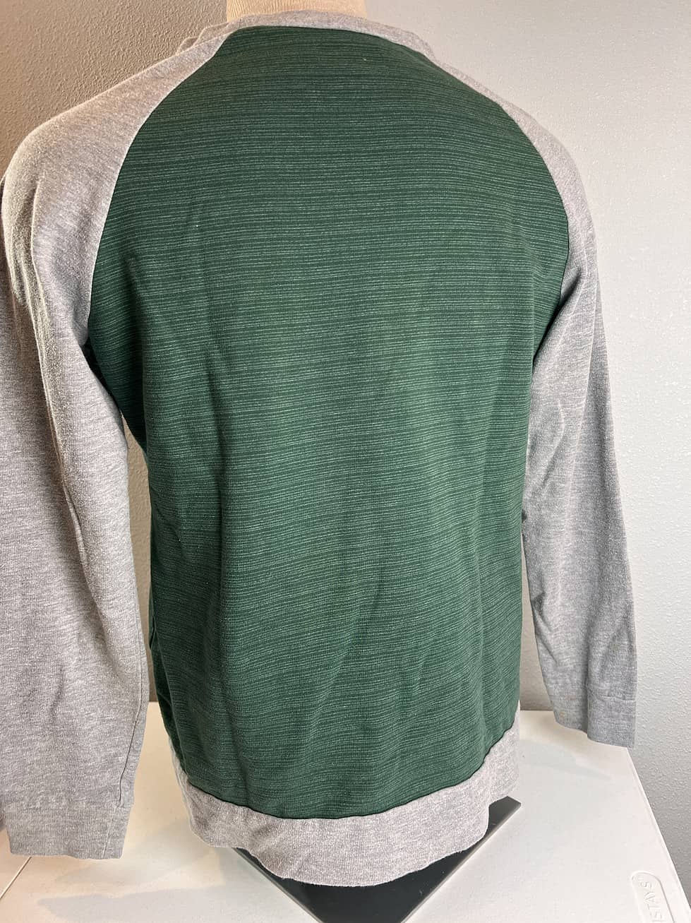Back view of a two-toned New York Jets sweatshirt, predominantly dark green with heather grey sleeves and bottom trim.