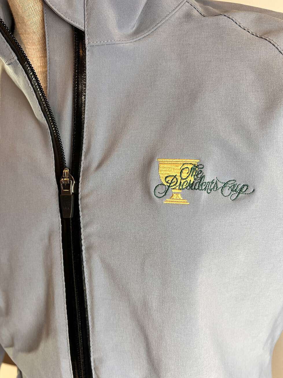 Close-up of the 2013 Presidents Cup logo embroidered in gold and green on the light grey fabric of the Sun Mountain rain jacket.