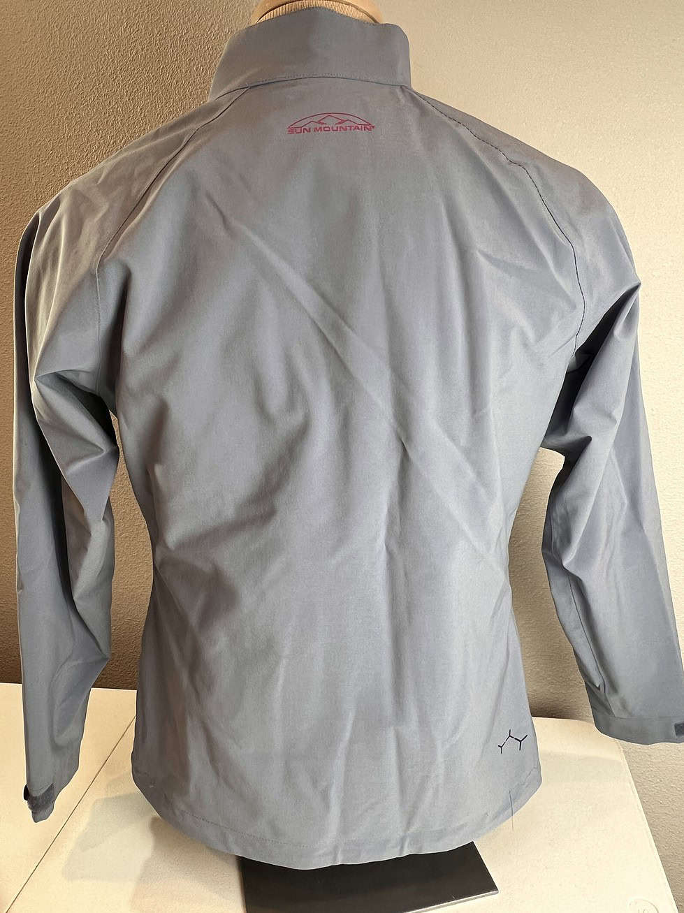 Back view of the light grey Sun Mountain rain jacket, showing a clean and seamless design with a high collar for added protection.