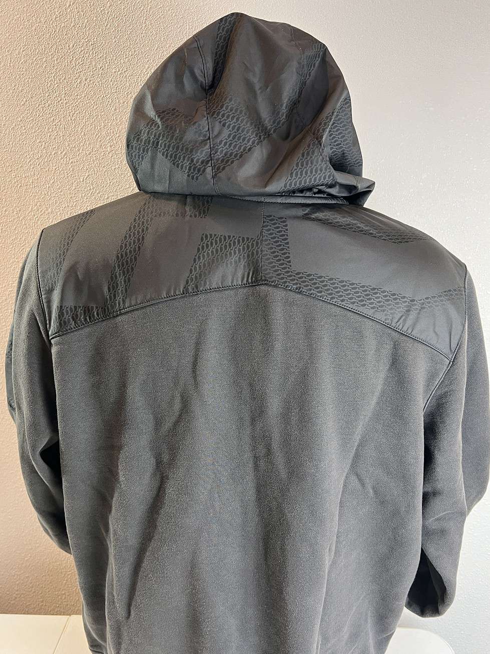 Back view of a charcoal grey Nike hoodie showcasing the rain-resistant textured upper back panel with a continuous design across the shoulders and a hood.