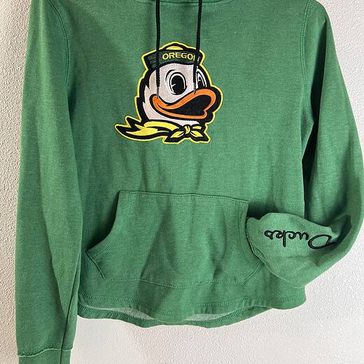 Full front view of a green University of Oregon sweatshirt with a large, embroidered mascot on the front, a front pouch pocket, and a signature on the sleeve, all complemented by a drawstring hood.