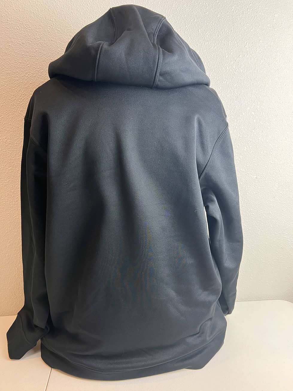 Back view of a black Under Armour youth hoodie, plain with no graphics, showcasing the seamless stitching and ribbed hemline.