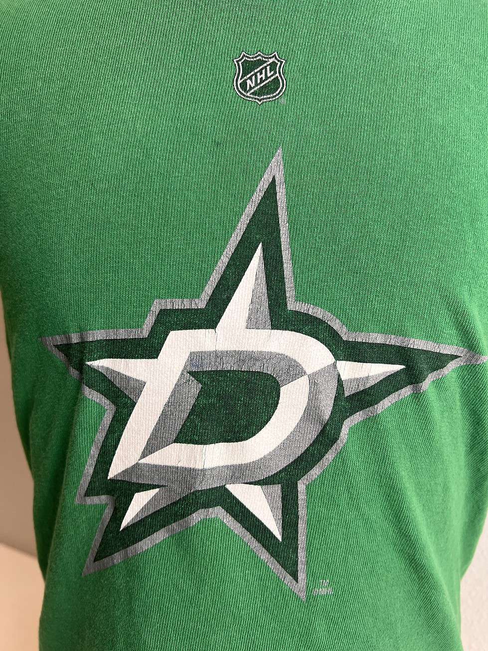 Close-up of the front of a green Reebok t-shirt featuring a large Dallas Stars logo, with NHL shield logo on the upper right.