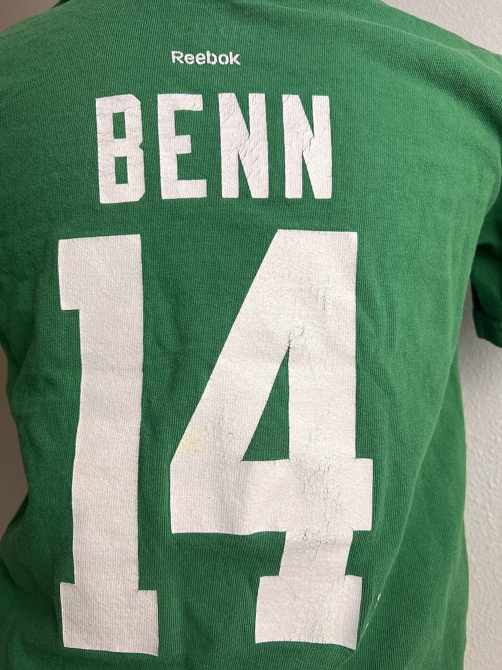 Back view of a child's green Reebok t-shirt with 'BENN 14' in large white letters. Details show cracking in print and small yellow spot in number 4.