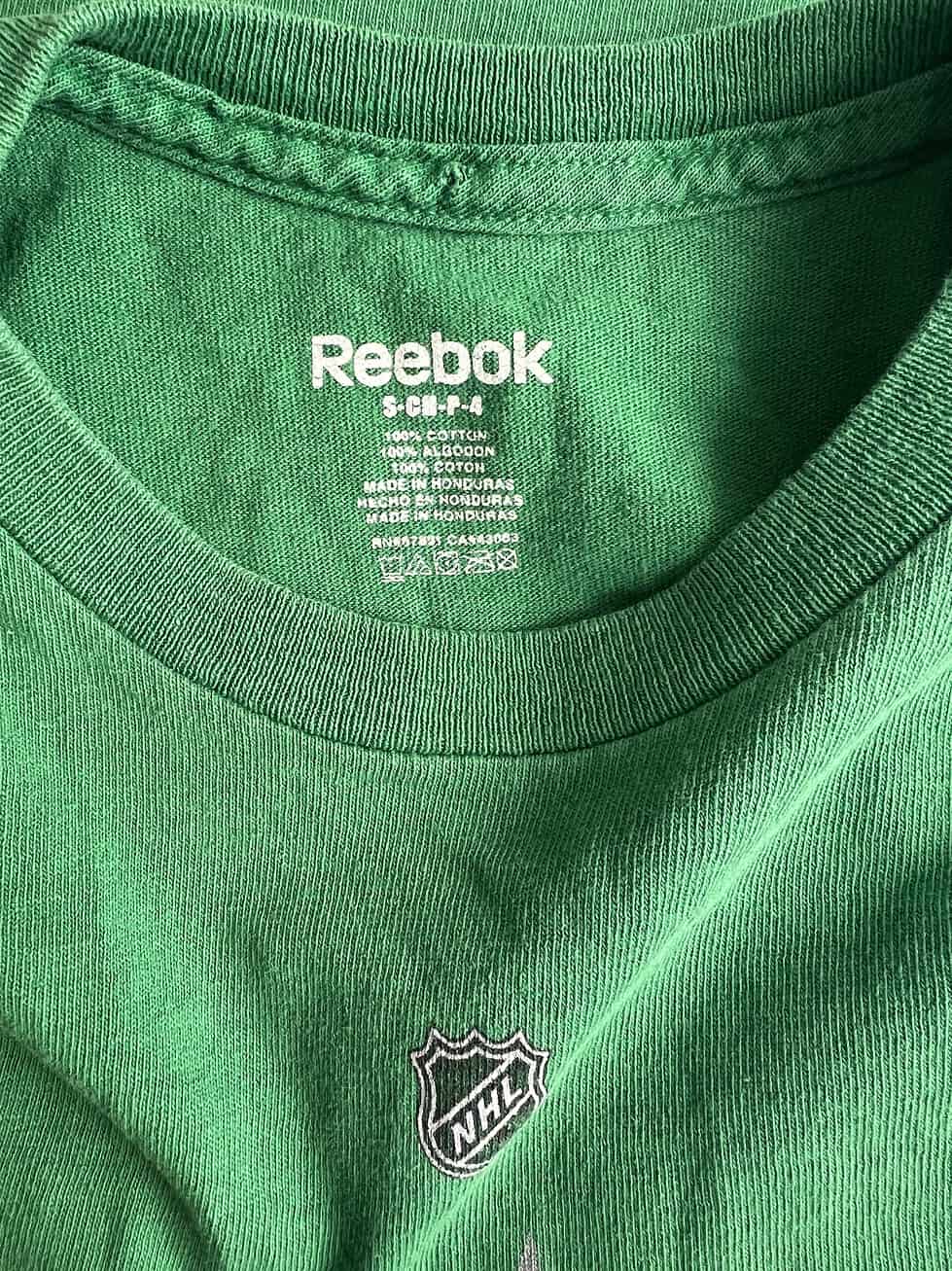 Close-up of a child's Reebok t-shirt label showing size as 'Child Small' and material as '100% Cotton', with NHL logo, indicating it's an official merchandise