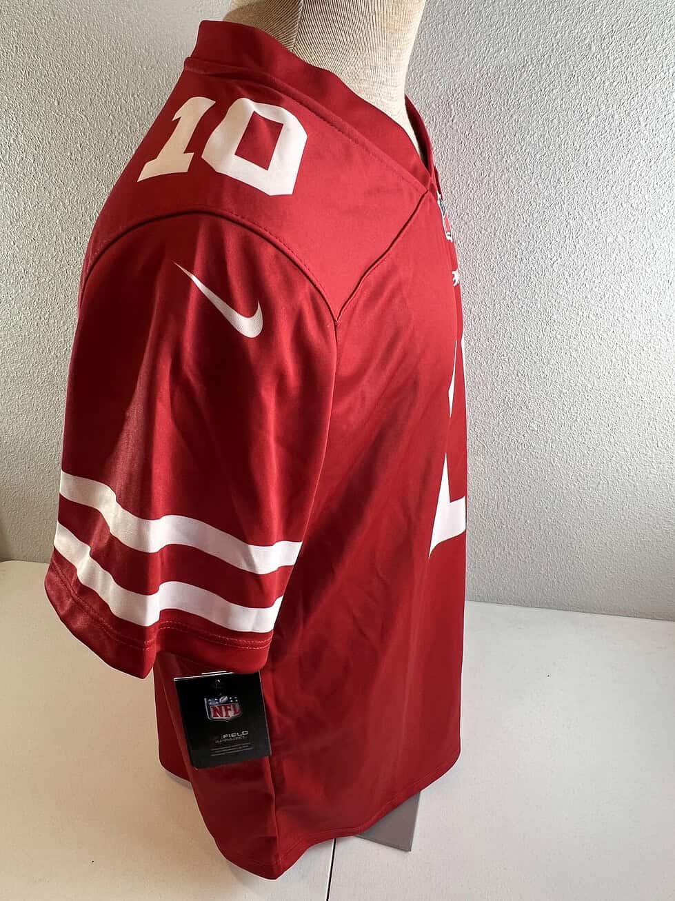 view of a women’s San Francisco 49ers jersey in red, featuring the number ‘10’ and a small NFL logo at the V-neck collar.