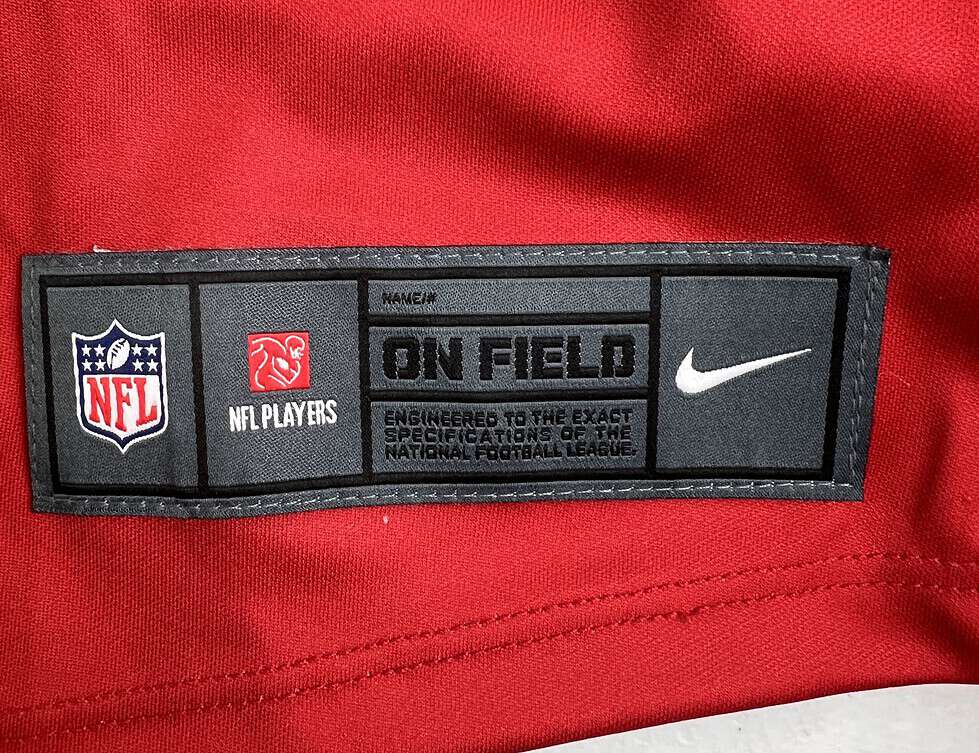 Detail of the lower tag on the jersey displaying NFL and NFLPA logos. Text reads “ON FIELD” style.