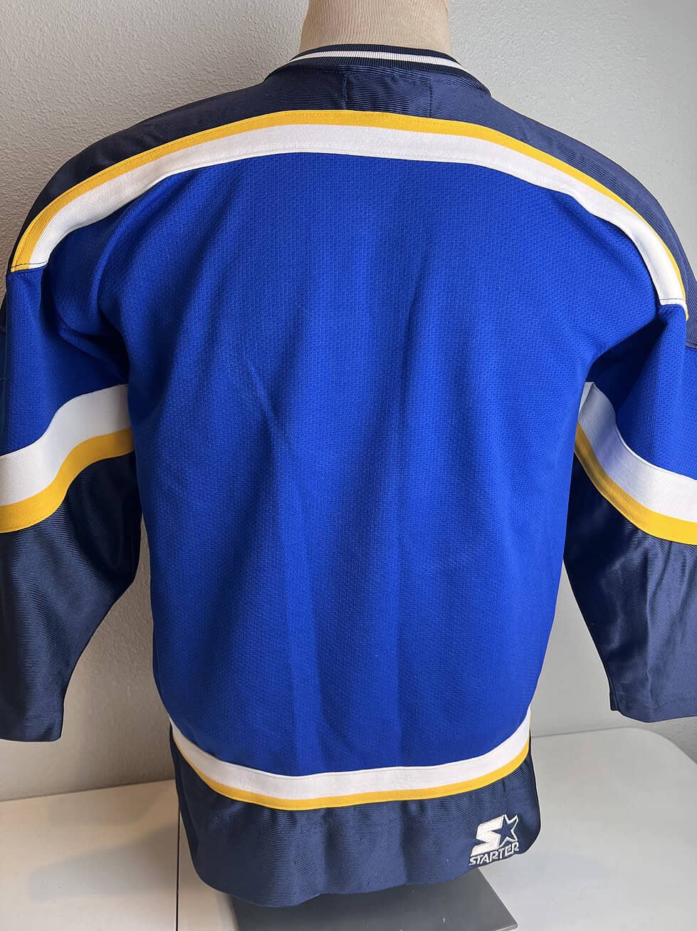 Back view of the blue St. Louis Blues hockey jersey with yellow and white stripes at the hem and on the sleeves