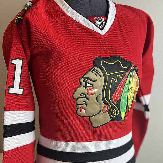 Front view of a Chicago Blackhawks red Reebok CCM jersey with large team logo on the front and number ‘1’ on the sleeve.