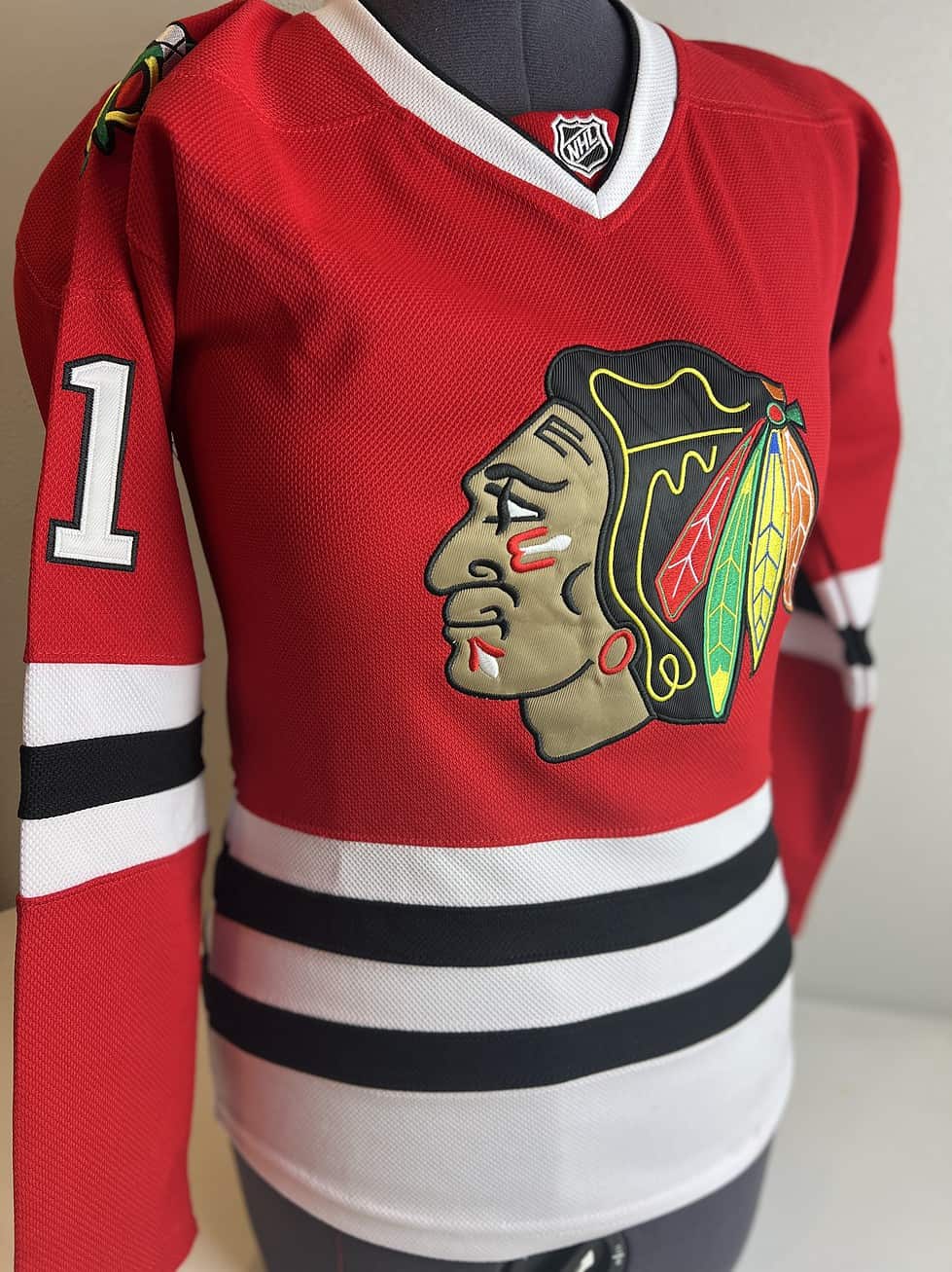 Front view of a Chicago Blackhawks red Reebok CCM jersey with large team logo on the front and number ‘1’ on the sleeve.