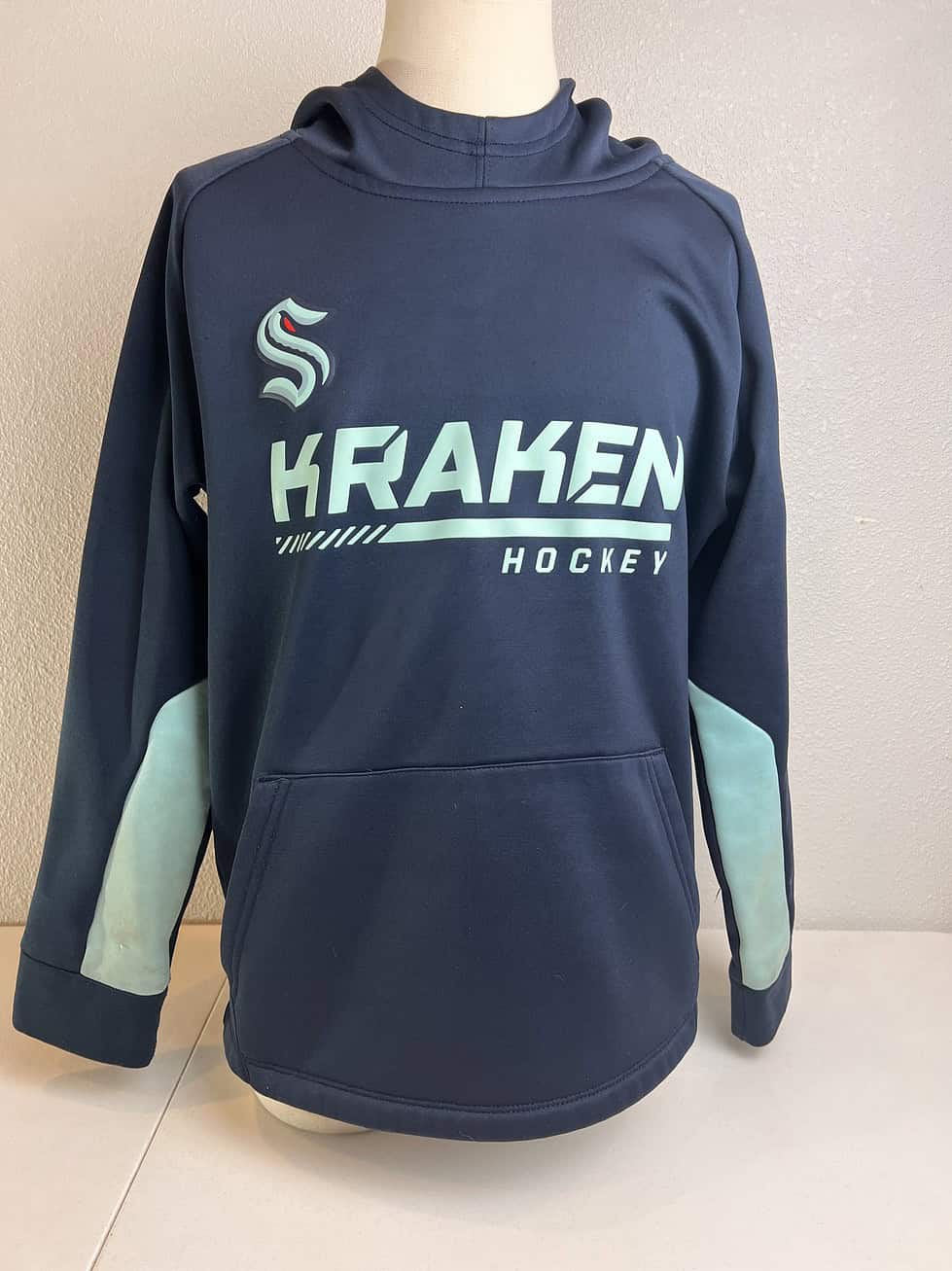 Youth size 8 Seattle Kraken hoodie in navy blue with the team's logo on the front and teal accents on the sleeves
