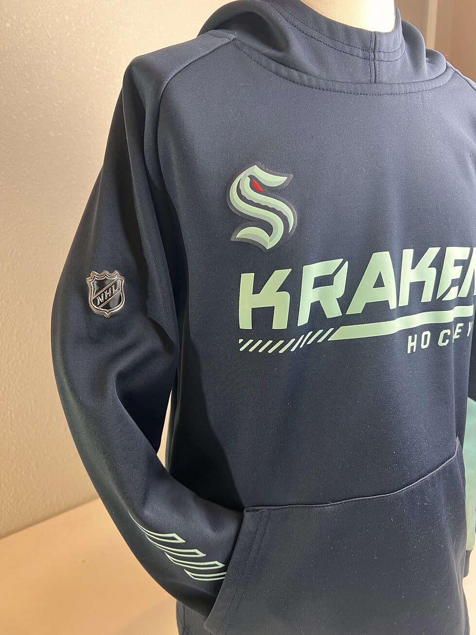 Close-up of the left sleeve of a Seattle Kraken hoodie showing the team's secondary logo and the NHL shield