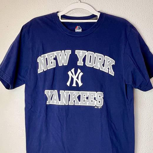 Navy blue New York Yankees t-shirt laid flat, displaying the team's logo in large, distressed white letters across the chest.