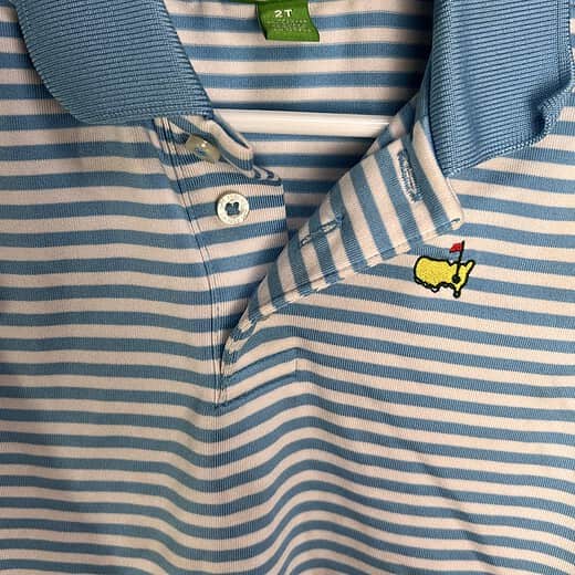 Close-up of the Masters logo on a blue and white striped polo shirt with collar detail.