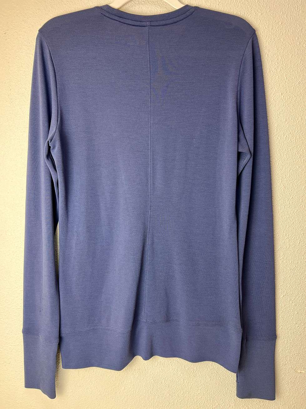 Rear view of a blue Nike Golf long-sleeve pullover, hanging on a white hanger against a light background