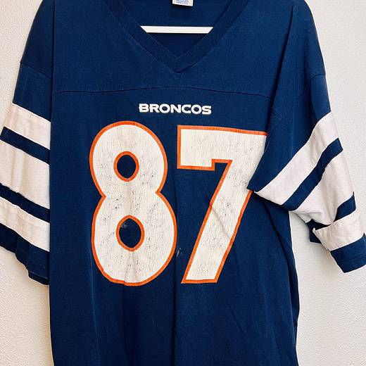 Front view of vintage Denver Broncos Ed McCaffrey jersey with a white number 87 outlined in orange.