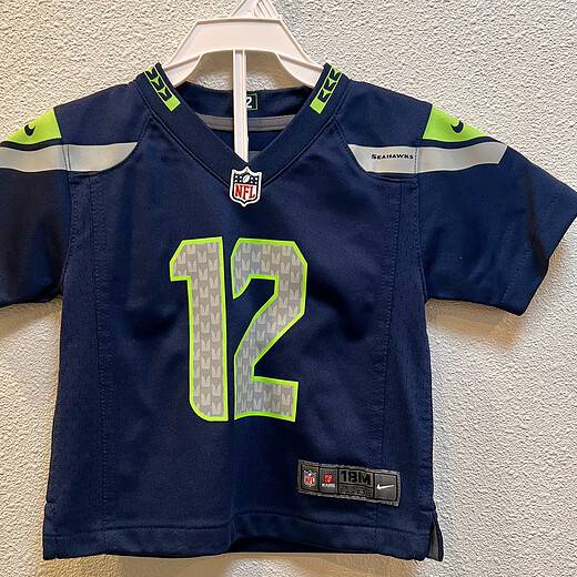 Front view of Seattle Seahawks toddler jersey in navy blue. The number 12 on front is in silver with neon green outline. NFL crest and jersey patch included.