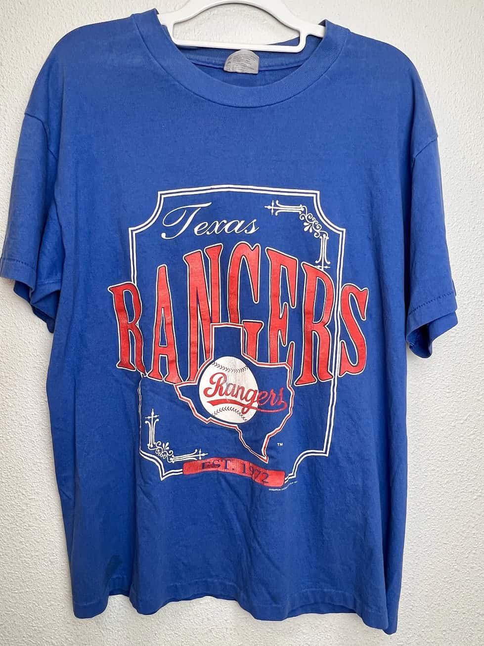Front view of vintage Texas Rangers royal blue tee, with the words Texas Rangers in large print. A Texas outline and baseball are part of the design. The words "Est. 1972" signify the team's beginning.