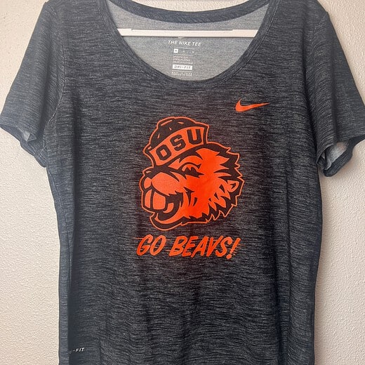 Front view of a Nike Dri-FIT Oregon State Beavers women’s T-shirt in heathered black, featuring a bright orange Benny Beaver graphic and “GO BEAVS!” slogan.