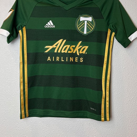Front view of a Portland Timbers Adidas youth jersey in green and gold with Alaska Airlines sponsor