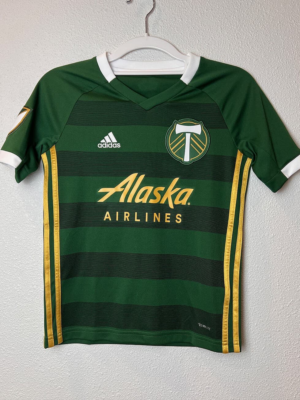 Front view of a Portland Timbers Adidas youth jersey in green and gold with Alaska Airlines sponsor