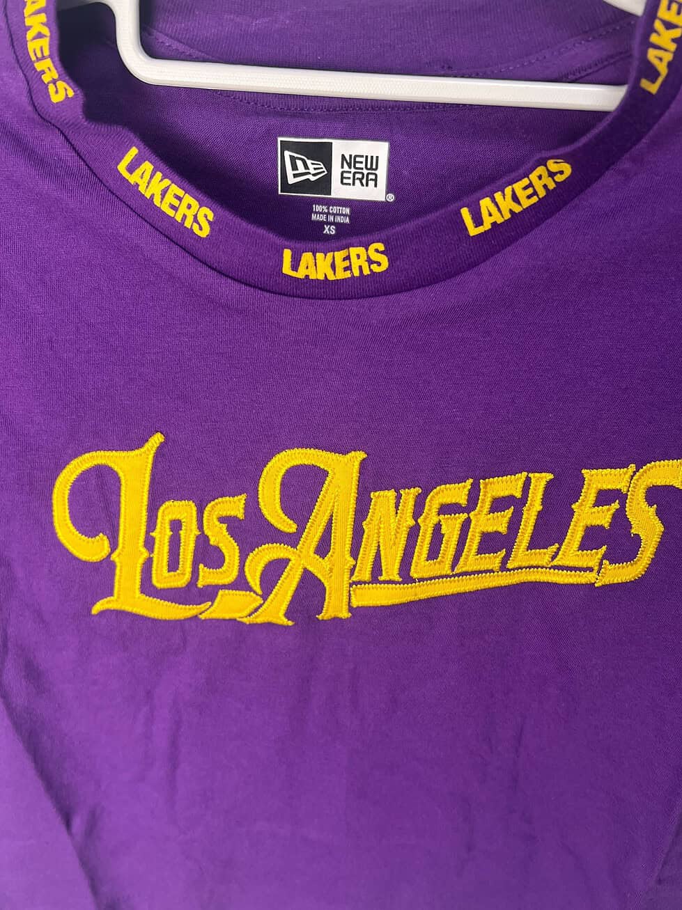 Close-up of the front logo and collar detail on a purple Los Angeles Lakers women’s crop tee by New Era.