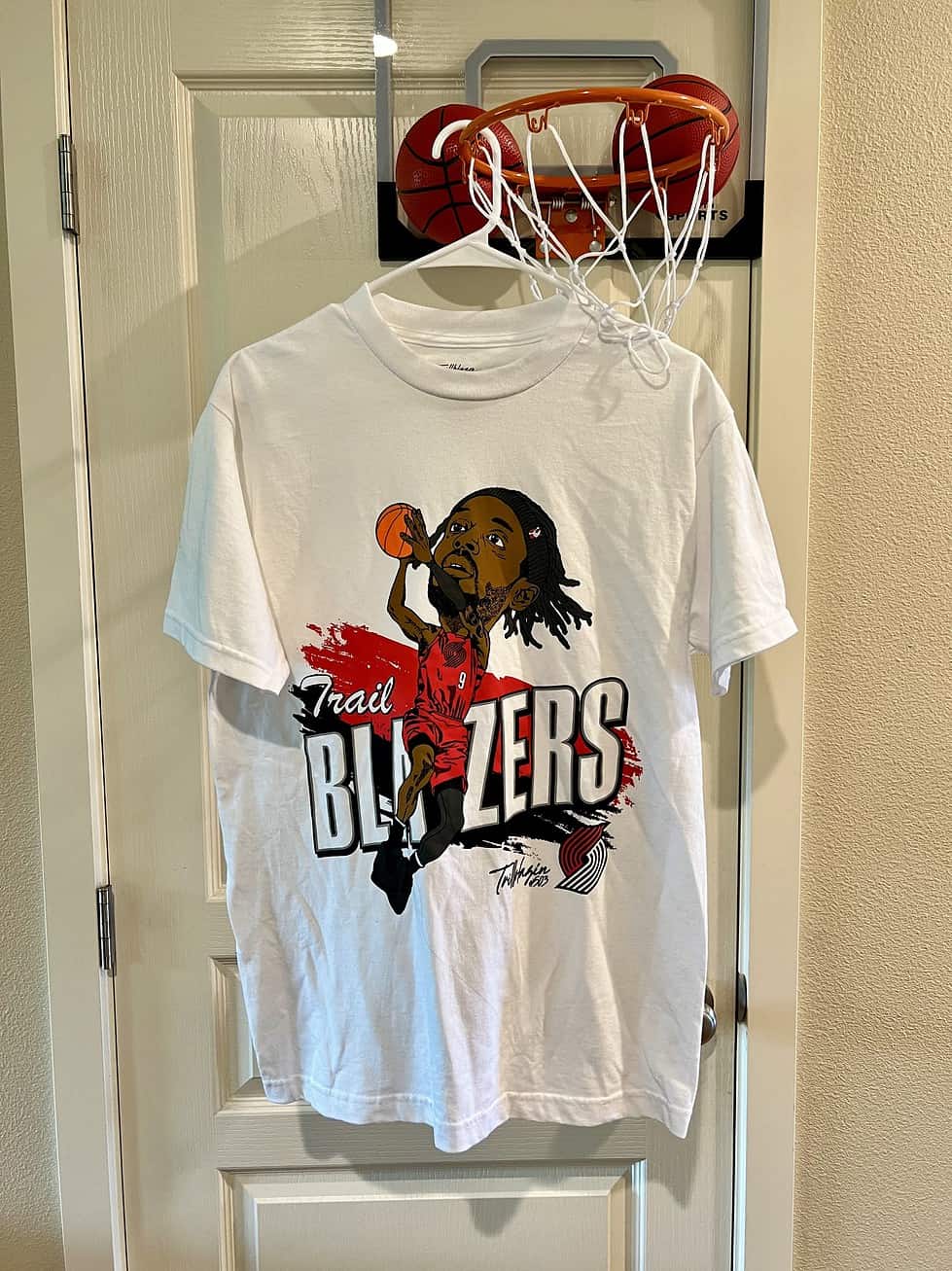 Full view of white Trail Blazers t-shirt with a caricature graphic of a player in action.