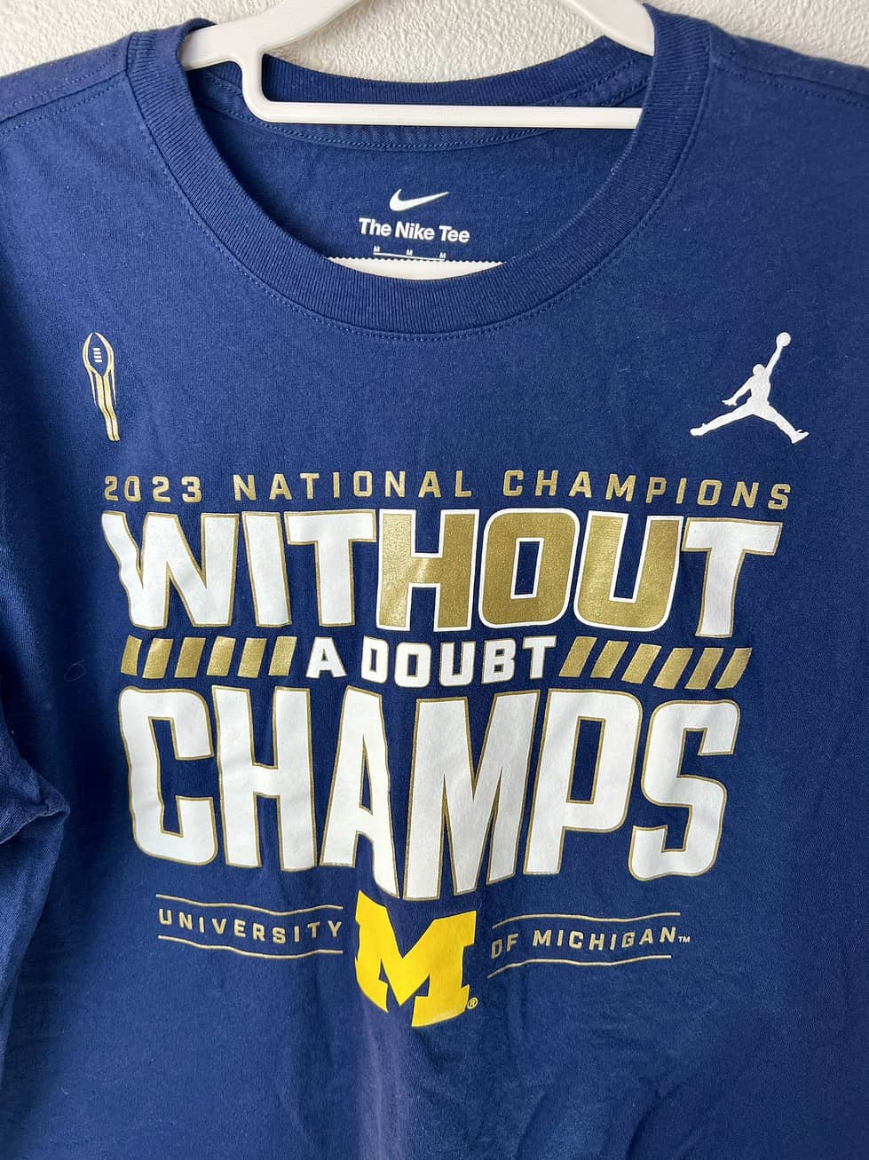 Close-up of “Without a Doubt Champs” text and logos on Michigan football t-shirt.