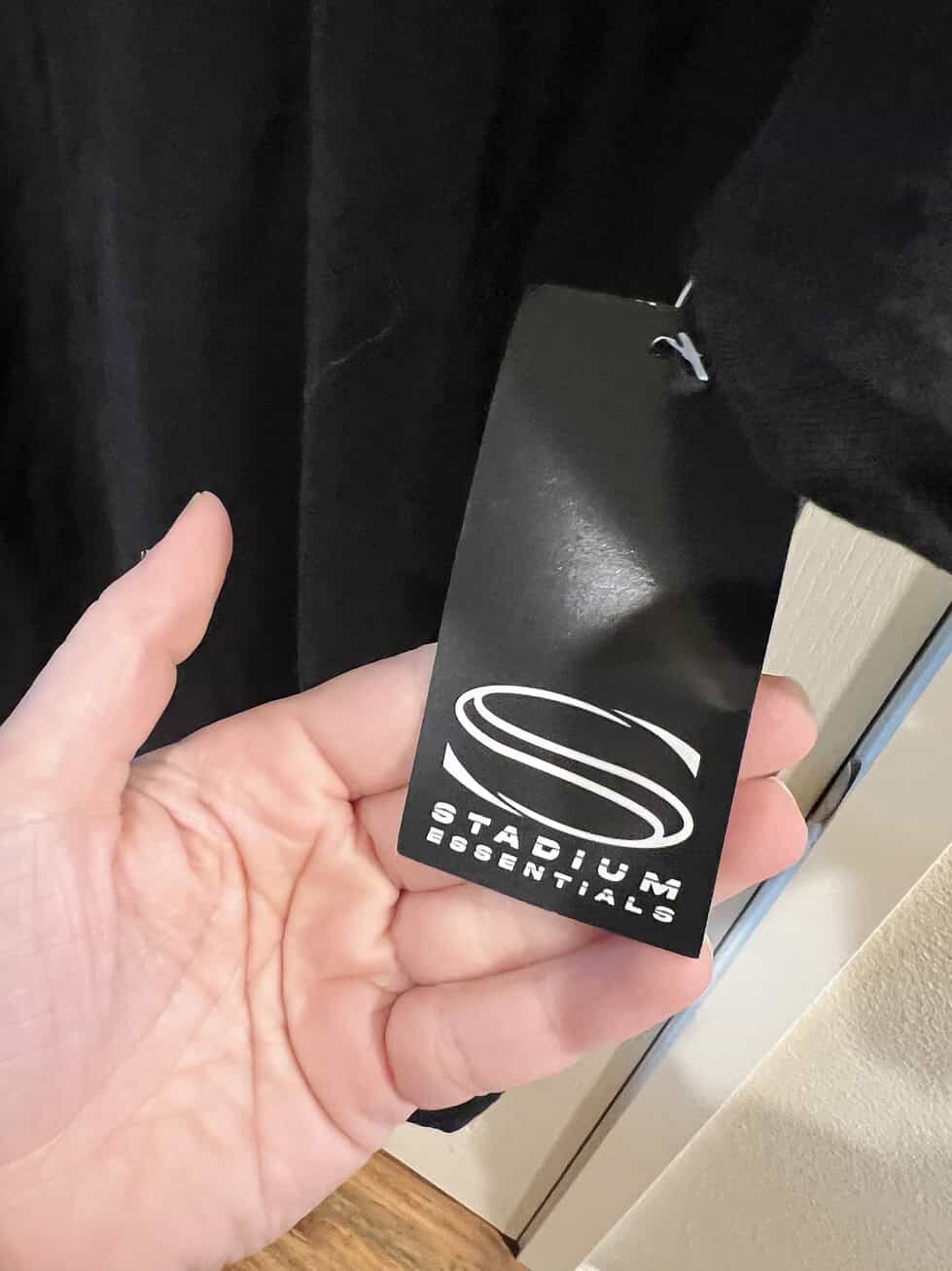 Close-up of Stadium Essentials brand tag attached to a black "Reign" T-shirt from Megan Rapinoe's retirement celebration.
