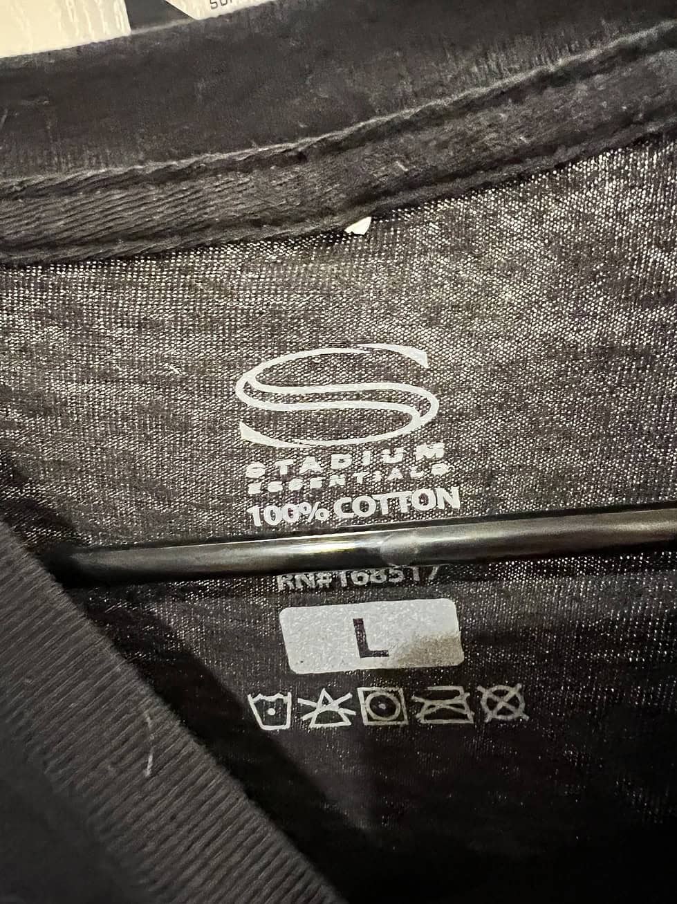Interior neck label of a black Stadium Essentials T-shirt, showing size Large and 100% cotton material.