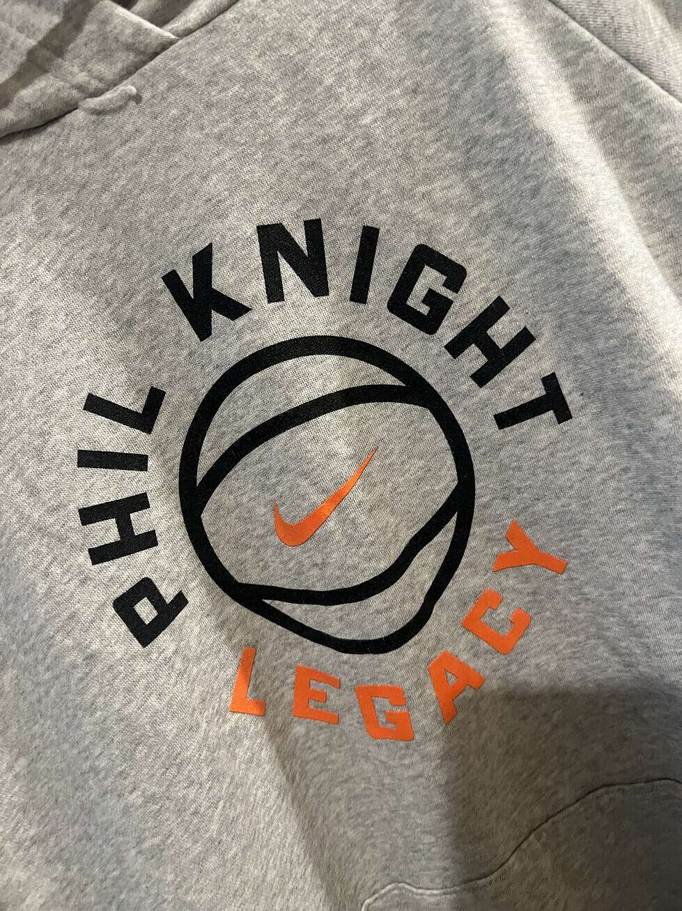 Detailed view of the "Phil Knight Legacy" graphic with basketball and orange Nike Swoosh.