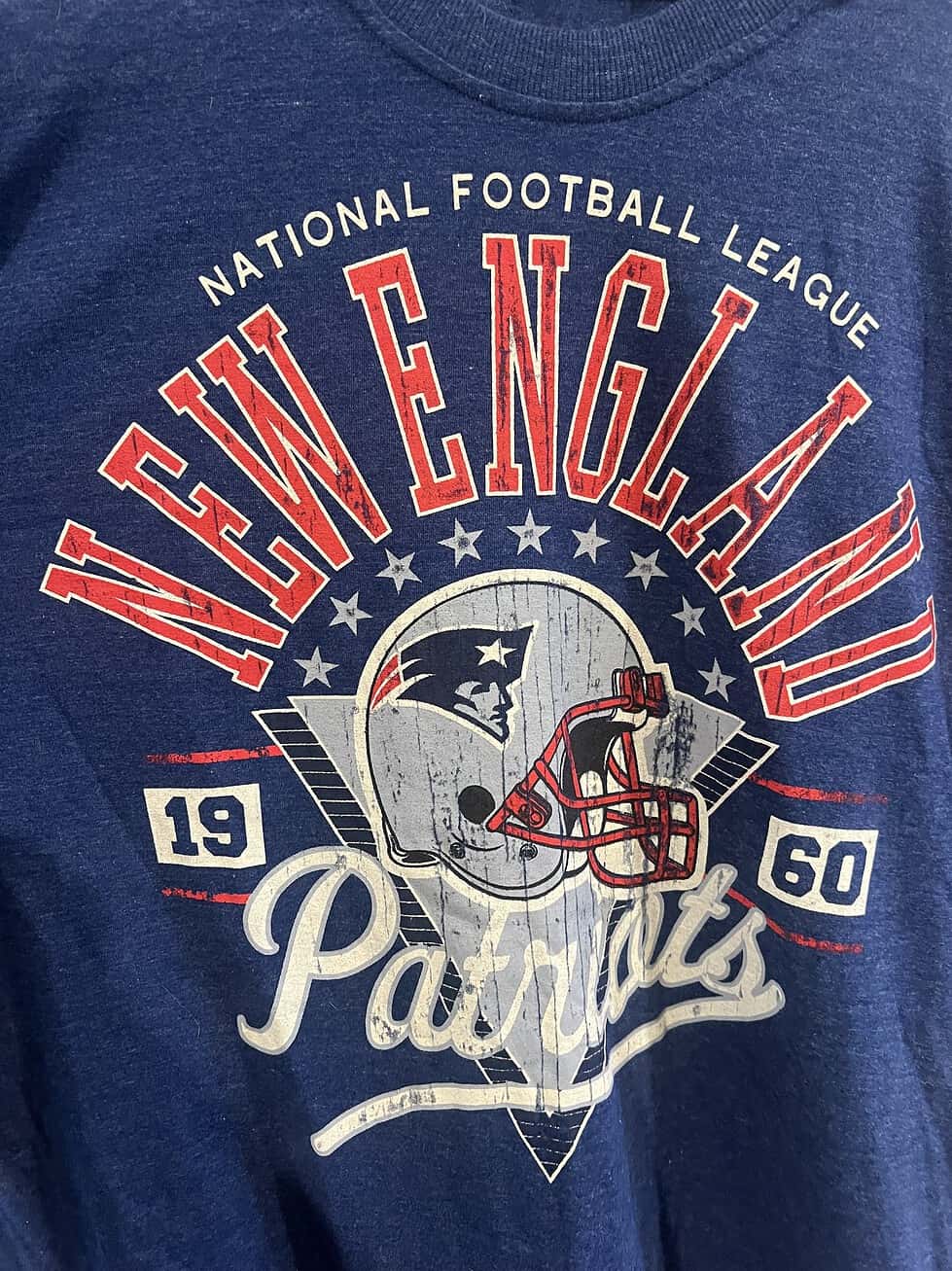Detailed front view of a New England Patriots T-shirt with a distressed helmet graphic and bold text.