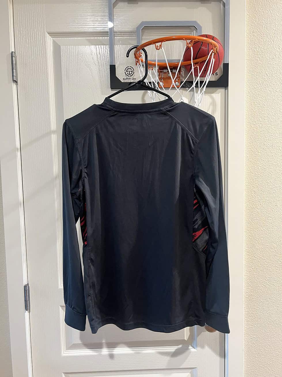 Back view of a black long sleeve Washington State University youth performance shirt hanging from a basketball hoop.
