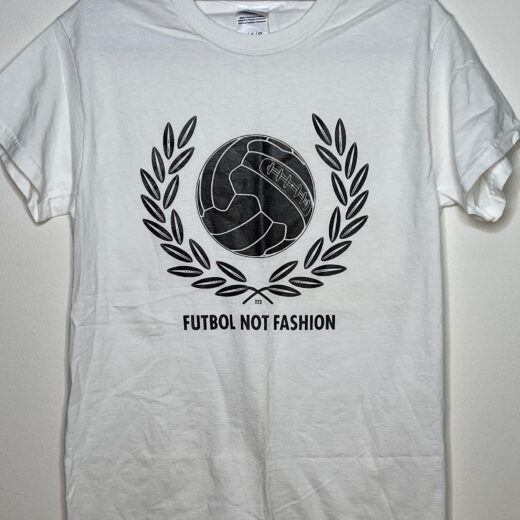 Front of t-shirt. Text says Futbol not Fashion. Image is a white and grey ball with branches on either side