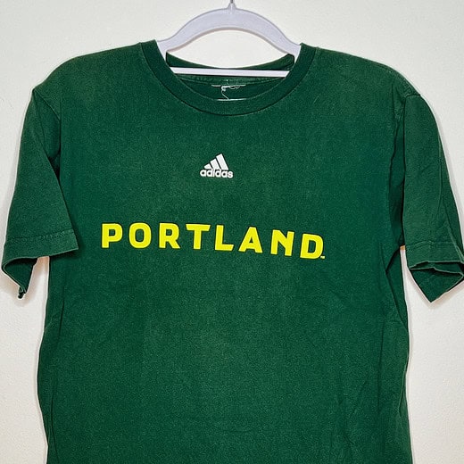 Front of Timbers green t-shirt with yellow text "Portland" and white adidas logo