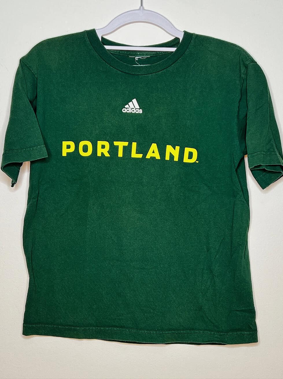 Front of Timbers green t-shirt with yellow text "Portland" and white adidas logo