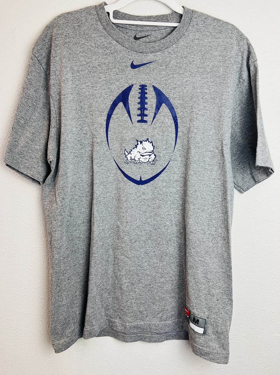 Gray Nike TCU football shirt with purple football graphic and Horned Frog logo on the front,