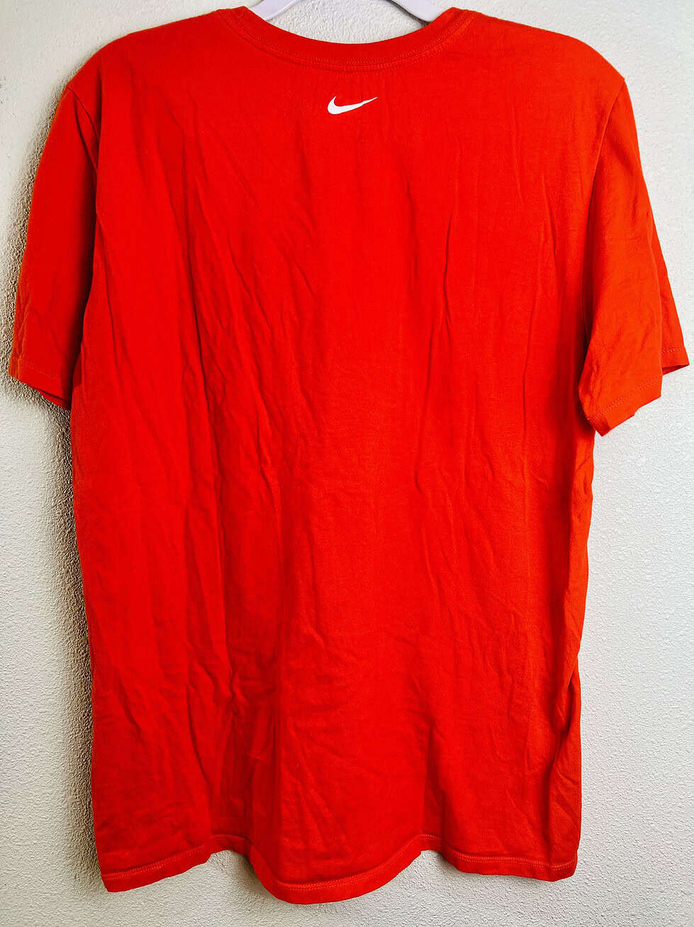 Back view of orange Nike t-shirt with white Swoosh logo on the upper back.
