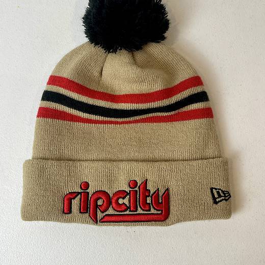Front view of tan Rip City New Era beanie with red "ripcity" embroidery and black pom.