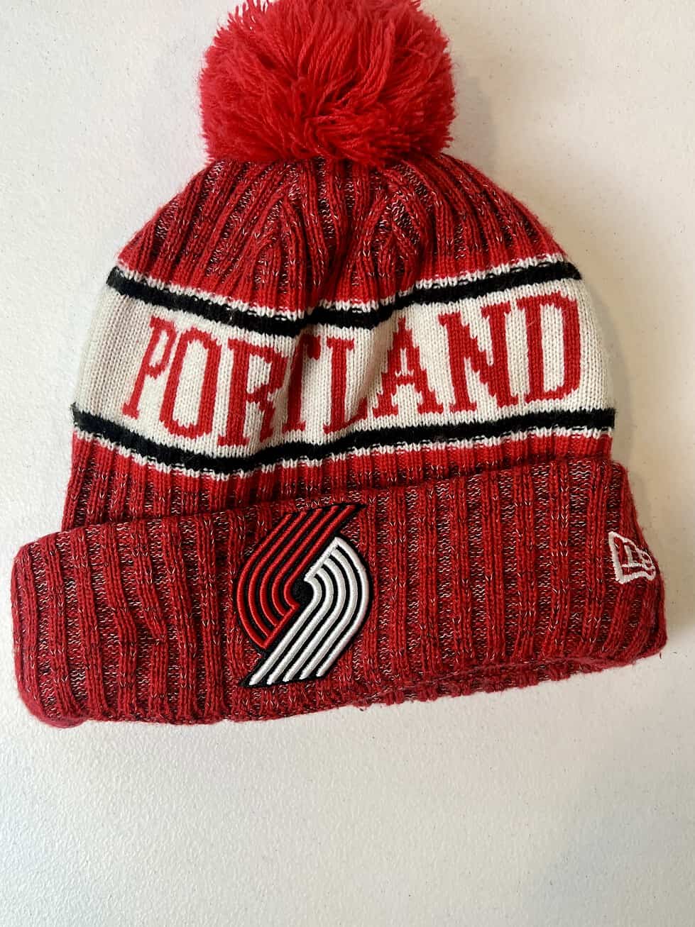 Front view of Trail Blazers New Era beanie with "PORTLAND" knit design and pom on top.
