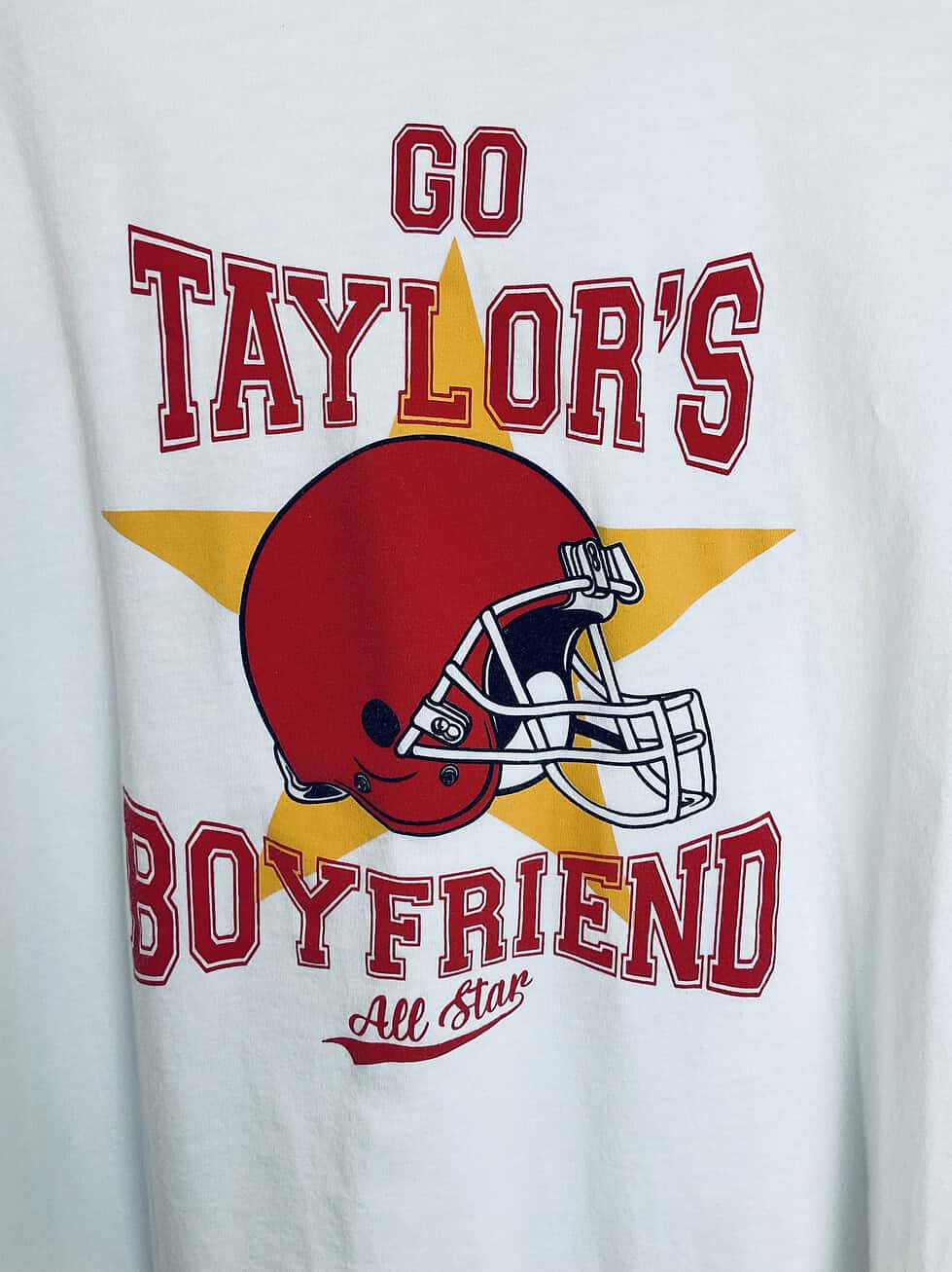 Close-up of text reading “Go Taylor’s boyfriend” and red football helmet graphic on the shirt.