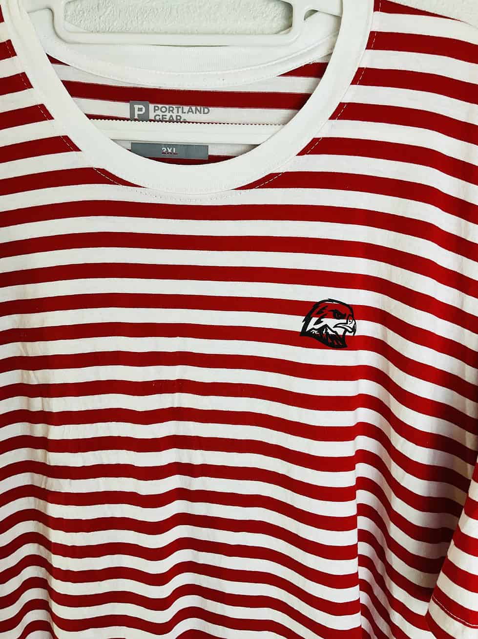 Close-up of Portland Winterhawks embroidered logo on chest of red and white striped t-shirt.